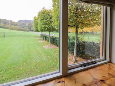 A view of a green lawn and trees through a window with a wooden windowsill at Fairoaks Barns in Hollybush near Ledbury