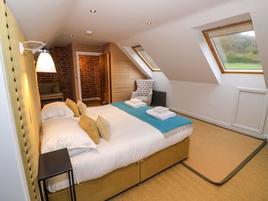 A bedroom with a bed and pillows skylight windows and an armchair at Fairoaks Barns Hollybush near Ledbury