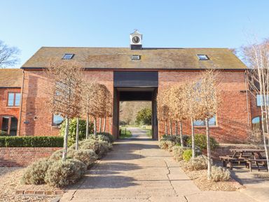 A driveway lined with trees leading to a brick building with a clock tower at Fairoaks Barns in Hollybush near Ledbury