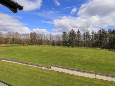 A grassy yard with a low wall and trees in the background under a partly cloudy sky at Mallard Cottage in Penrith