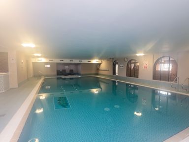 An indoor swimming pool with tiled floor and chairs at the far end at Mallard Cottage in Penrith
