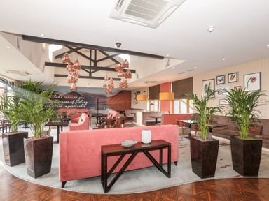 A lounge area with pink and brown sofas wooden tables potted plants and pendant lights at Mallard Cottage in Penrith