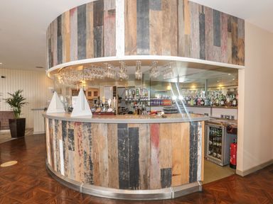 A curved bar counter with hanging glasses bottles and a fire extinguisher behind it at Mallard Cottage in Penrith