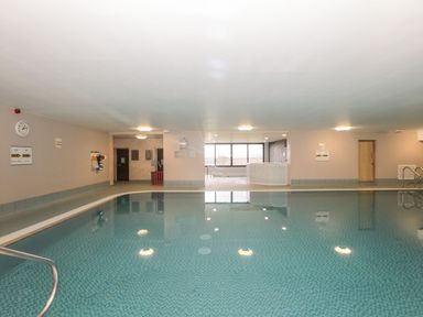 An indoor swimming pool with a hot tub area and windows at Mallard Cottage in Penrith