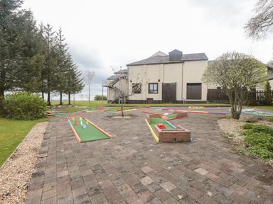 An outdoor mini golf course with a two story building and trees in the background at Mallard Cottage in Penrith