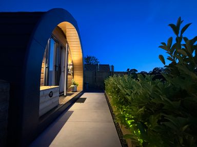 A curved wooden cabin with a path and bushes illuminated at night at No Deer in Ashbourne