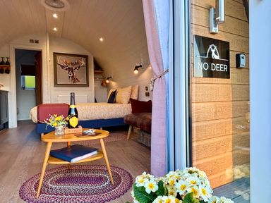 A bedroom with a bed, wooden table with a bottle and flowers, a deer painting, and a sign reading No Deer at No Deer in Ashbourne