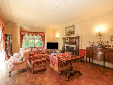 A living room with wooden furniture a fireplace large windows and red patterned curtains at Highcliffe Manor in Flamborough