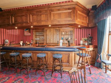 A bar area with wooden stools and a counter in a room with red striped wallpaper and blue curtains at Highcliffe Manor in Flamborough
