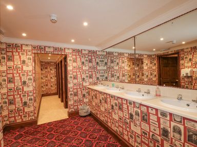 A bathroom with four sinks a large mirror red patterned carpet and walls covered in pictures at Highcliffe Manor in Flamborough