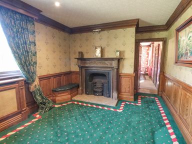 A room with a fireplace a green patterned carpet a window with green curtains and wooden paneling at Highcliffe Manor in Flamborough