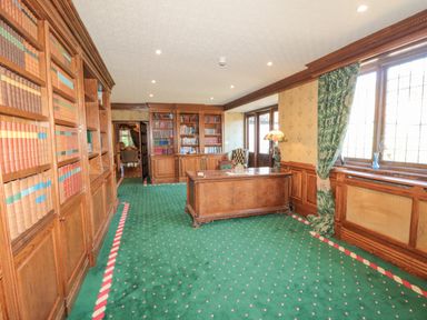 A room with wooden bookshelves filled with books a wooden desk a green carpet and large windows at Highcliffe Manor in Flamborough
