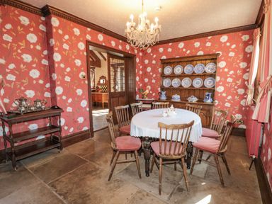 A dining room with a round table and six wooden chairs with cushions a chandelier and a wooden cabinet with blue and white plates at Highcliffe Manor in Flamborough
