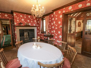 A dining room with a round table covered with a white tablecloth surrounded by wooden chairs next to a fireplace with floral wallpaper at Highcliffe Manor in Flamborough