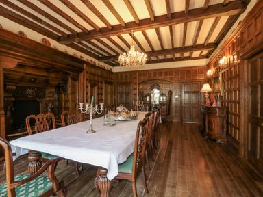 A dining room with a long table covered by a white tablecloth surrounded by wooden chairs with green cushions and a chandelier overhead at Highcliffe Manor in Flamborough