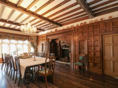 A dining room with a long table and chairs a chandelier wooden paneling and a fireplace at Highcliffe Manor in Flamborough