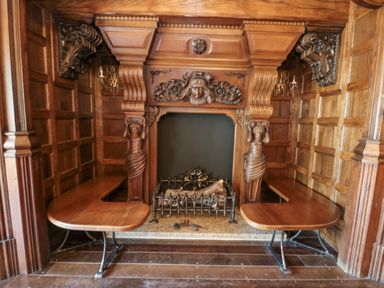 A wooden fireplace with carved figures on either side and wooden benches on both sides at Highcliffe Manor in Flamborough