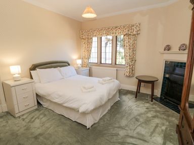 A bedroom with a double bed two bedside tables lamps a window with floral curtains a small round table and a fireplace at Highcliffe Manor in Flamborough