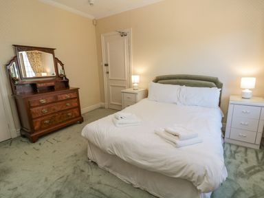 A bedroom with a bed with white linens two bedside tables with lamps and a wooden dresser with a mirror at Highcliffe Manor in Flamborough