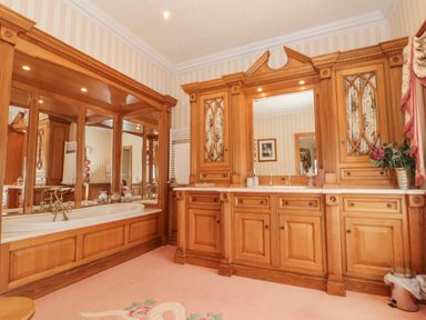 A bathroom with wood paneling around a bathtub and wooden cabinetry with a large mirror at Highcliffe Manor in Flamborough