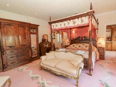 A bedroom with a four-poster bed, wooden wardrobe, dressing table, and upholstered sofa at Highcliffe Manor in Flamborough