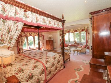 A bedroom with a four poster bed floral curtains sitting area with chairs and ottoman and a large wooden wardrobe at Highcliffe Manor in Flamborough