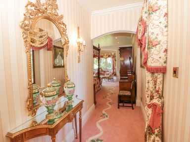 A hallway with a gold framed mirror and decorative vases on a glass table at Highcliffe Manor in Flamborough