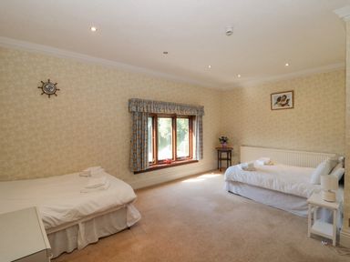 A bedroom with two single beds a window with curtains a side table with a lamp and a small round table with flowers at Highcliffe Manor in Flamborough