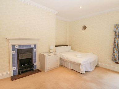 A bedroom with a bed a white dresser a fireplace and a window with patterned curtains at Highcliffe Manor in Flamborough