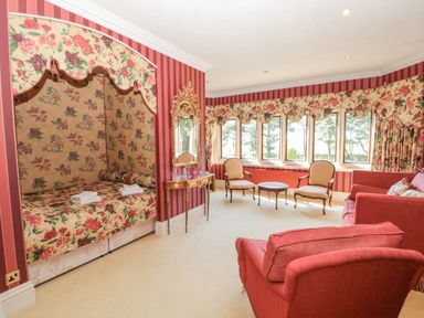 A sitting room with floral canopy bed armchairs and a small table by a window at Highcliffe Manor in Flamborough