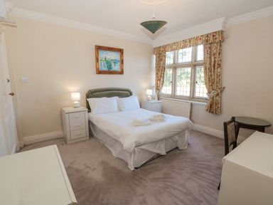 A bedroom with a double bed with white linens two bedside tables with lamps a painting above the bed a window with floral curtains and a small table with a chair at Highcliffe Manor in Flamborough