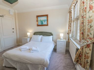 A bedroom with a double bed with white bedding two nightstands lamps floral curtains and a framed painting at Highcliffe Manor in Flamborough