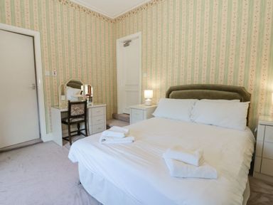 A bedroom with a bed with white linens and folded towels a vanity with a chair two closed doors and bedside tables with lamps at Highcliffe Manor in Flamborough