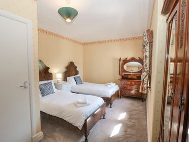 A bedroom with two single beds a bedside table a lamp a wooden dresser with mirror wooden wardrobe and patterned curtains at Highcliffe Manor in Flamborough