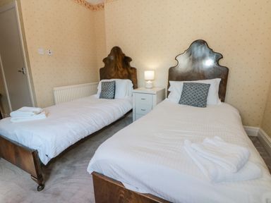 A bedroom with two single beds white bedding and dark wooden headboards and a bedside table with a lamp at Highcliffe Manor in Flamborough