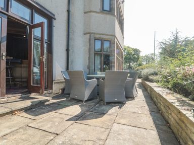 A stone patio with outdoor chairs and a table next to a building with open wooden doors at Highcliffe Manor in Flamborough