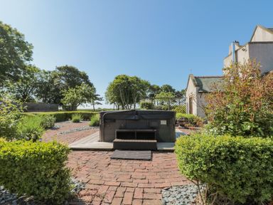 An outdoor hot tub with steps on a brick patio surrounded by bushes and plants at Highcliffe Manor in Flamborough