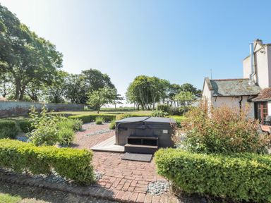 An outdoor garden area with hedges a brick pathway a hot tub and a white house at Highcliffe Manor in Flamborough