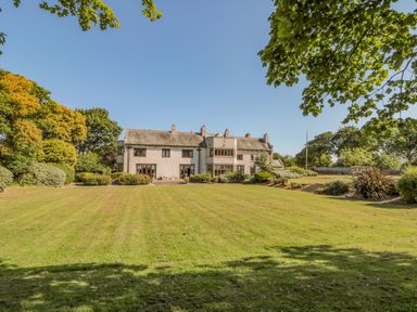 A large house with multiple windows and a tiled roof surrounded by a lawn and trees at Highcliffe Manor in Flamborough