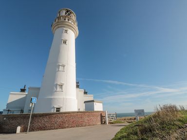 A white lighthouse with a brick wall and a no exit sign near a path leading to the sea at Highcliffe Manor in Flamborough