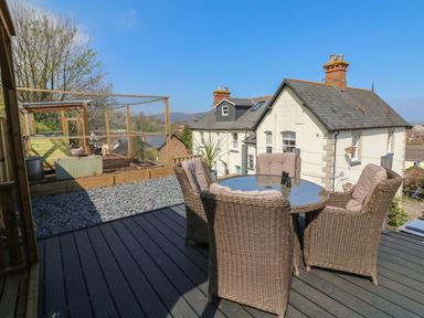 An outdoor deck with a round glass table and four wicker chairs with cushions at The Outlook in Minehead