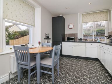 A kitchen with a round wooden table and four chairs a tall black cabinet a microwave a sink and patterned floor tiles at The Outlook in Minehead