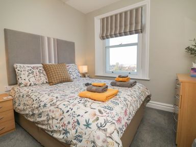 A bedroom with a bed with patterned bedding and folded towels on top next to a window with striped blind at The Outlook in Minehead