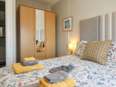 A bedroom with a bed covered in patterned bedding and folded towels on it with a wooden wardrobe and bedside lamp at The Outlook in Minehead