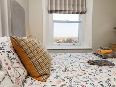 A bedroom with a bed with animal and floral patterned bedding and folded towels on the bed near a window with a view at The Outlook in Minehead