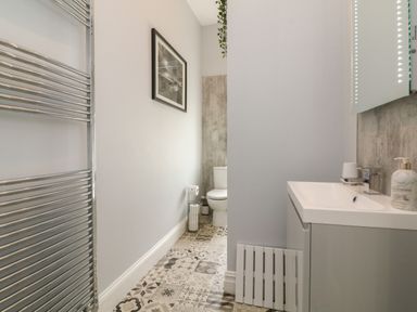 A bathroom with a toilet, patterned floor tiles, a sink with soap dispenser, a wall-mounted towel rail, and a framed picture at The Outlook in Minehead