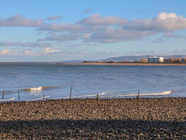 A rocky beach with wooden sticks near the shoreline and a body of water with a distant land and buildings at The Outlook in Minehead