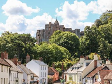 A street with shops and houses with a castle on a hill surrounded by trees at The Outlook in Minehead