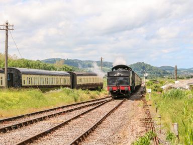 A steam train moving on railway tracks with hills and greenery in the background at The Outlook in Minehead