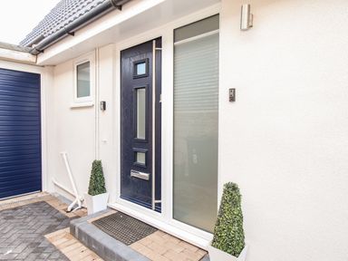 A front door with glass panels flanked by two potted plants and a garage door at The White House in Weymouth